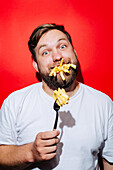 A playful scene with chips on a fork and in a man's mouth against a striking red background. The humorous scene captures the mood of a cheerful barbecue party.