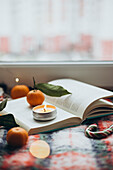 Warm and inviting Christmas scene with a burning candle on an open book, surrounded by fresh mandarins and a candy cane, conveying a feeling of Christmas spirit and relaxation.
