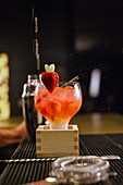 A professional bartender skilfully prepares a lively cocktail in a chic bar. The drink is garnished with a fresh strawberry and emphasises the lively atmosphere.