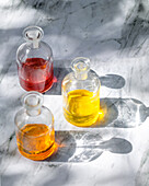 Top view of natural body oils infused with plants such as calendula and rose. The image captures the bright colours of the oils in glass bottles that cast shadows.