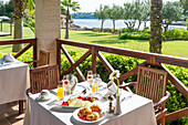 Charming al fresco dining on a hotel terrace overlooking the sea and lush garden Wooden chairs, elegant crockery and lush greenery create a tranquil, luxurious atmosphere