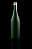 A slender wine bottle made of green glass stands upright on a reflective surface against a black background that emphasises its elegant shape and minimalist design. Perfect for presenting drinks.