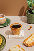 A cosy breakfast scene with a ceramic cup of black coffee, toast with peanut butter and banana slices, almonds and a potted plant in a warm, inviting ambience.
