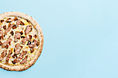 Top view of a gourmet pizza with roast duck fillet, figs, almonds and truffle sauce, beautifully presented on a pastel blue background that adds a touch of elegance to the casual meal.