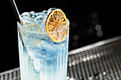 Refreshing Tom Collins cocktail, served in a tall glass with a straw and garnished with a slice of dried lemon - perfect for a summer party or a relaxed evening