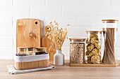 Wooden chopping boards stand on a modern kitchen worktop next to elegant jars filled with pasta and grains, accentuated by a white brick wall.
