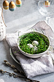 A fresh Easter decoration with painted eggs in a ceramic bowl, delicately embedded in green grass and complemented by subtle spring accents. This composition radiates the spirit of rebirth and renewal associated with Easter.