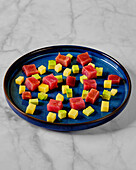 Ein lebhaftes Arrangement aus gewürfeltem Thunfisch, Mango und Avocado auf einem blauen Teller vor einem Marmorhintergrund hebt die frischen Zutaten und die kulinarische Präsentation hervor