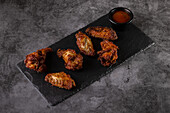 Savoury, crispy chicken wings on a slate, paired with a rich sauce in a black bowl. An appetising display that is perfect for presenting dishes and menus.