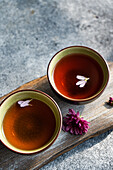 Two elegant teacups filled with rich, amber-coloured tea are adorned with delicate petals The scene rests on a rustic wooden surface that emphasises the tranquil ambience