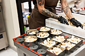 A determined baker with tattooed arms and black gloves arranges pastries in metal moulds, demonstrating his expertise and dedication in an authentic Italian bakery