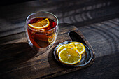 A cosy ambience with a glass of full-bodied, aromatic English tea and bright lemon slices on a rustic wooden table underlines a moment of relaxation.