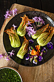 Courgette flowers with colourful edible flowers on a rustic wooden board for preparing a courgette tart. The bright colours of the flowers contrast beautifully with the green of the courgettes.