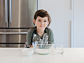 A young child, a budding chef, stands confidently at a kitchen table with baking ingredients at the ready. The child is wearing a starry apron and is getting ready to embark on a culinary adventure.