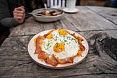 A delicious breakfast with fried eggs and ham is served at a rustic wooden table on the Geisleralm in the Dolomites. A warm setting for a cosy dining experience
