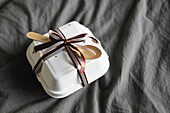 Top view of a bento birthday cake, elegantly wrapped and secured with a ribbon and wooden spoon, resting on a textured grey bed sheet.