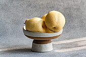 Three white Chinese pears are elegantly presented in a ceramic bowl against a textured background. The soft light emphasises their delicate texture and evokes freshness and simplicity.