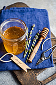 A jar of golden honey with a rustic wooden spoon and delicate sprigs of lavender rests on a blue napkin The arrangement evokes a natural and sweet aromatic theme