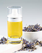 A glass bottle filled with lavender oil stands next to dried lavender flowers. The soothing essence of lavender provides relaxation and serenity and is perfect for a spa ambience.