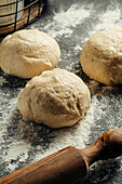 Three balls of dough lie on a floured surface, accompanied by a wooden rolling pin. The scene captures the essence of baking and is reminiscent of home-made dishes.