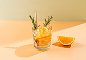 Ein ansprechendes Sommergetränk, garniert mit Rosmarin und Orange, vor einem zweifarbigen pastellfarbenen Hintergrund. Dieses Bild fängt die Essenz einer sommerlichen Erfrischung ein.