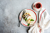 Top view of classic homemade apple waffles, topped with ripe apple slices, bananas and mint leaves, accompanied by a cup of coffee on a grey surface. Ideal for a refreshing breakfast set-up.