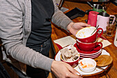 A person collects red cups with coffee grounds and plates on a wooden table in a coffee shop. This scene captures the bustling atmosphere of a speciality coffee shop.