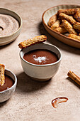 Homemade churros, dipped in rich chocolate sauce, sprinkled with sugar and cinnamon, presented on an atmospheric ceramic surface with a linen background.