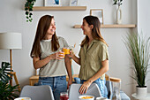 A lesbian couple share a joyful moment at home and toast with a glass of orange juice Surrounded by cosy furnishings, they celebrate love and togetherness LGBTQIA+ Pride