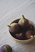 A rustic ceramic bowl filled with ripe, purple figs on a textured linen tablecloth that captures a natural and earthy ambience, ideal for culinary themes