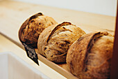 A selection of freshly baked, artisan breads displayed on a rustic wooden shelf in a bakery, showcasing their golden, crispy crusts and inviting aroma