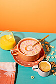 Top view of a lively breakfast scene with a bowl of muesli with milk, complemented by a fresh glass of orange juice and a cup of coffee on a colourful background.