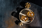 Top view of spiced cognac cocktails with cinnamon and star anise, accompanied by bowls of almonds, peanuts and hazelnuts, served on a rustic tray against a dark textured background.