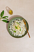 A green plate with creamy fusilli pasta, garnished with fresh sage leaves and Parmesan cheese. A bottle of olive oil and a golden fork complement the beige background.