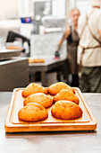 Golden brown pastries lie on a wooden tray in an Italian bakery, exuding warmth and inviting aromas Fuzzy bakers work diligently in the background, creating a cosy ambience