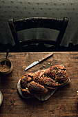 Top view of a freshly baked babka bread with chocolate and pistachios lying on a rustic wooden table next to a bowl of sugar and a knife. The image captures the rich texture of the bread and the cosy, homely background suggests a traditional baking environment.