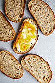 Draufsicht auf frisch geschnittenes hausgemachtes Sauerteigbrot mit Butter und Marmelade, serviert auf einer strukturierten Oberfläche.