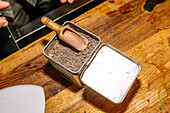 A wooden scoop in a metal container filled with cocoa nibs on a rustic wooden table. Perfectly captured for a coffee speciality that highlights gourmet elements.