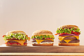 Three juicy cheeseburgers with lettuce, tomato and cheese on a wooden board Perfect for fast food lovers who want a fresh and appetising meal