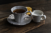 Ein klassischer englischer Tee in einer eleganten weißen Tasse mit Zitronenscheiben und etwas Milch in einer kleinen Kanne, präsentiert auf einem rustikalen Holztablett.
