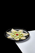 A gourmet dessert with fresh kiwi and pear slices, elegantly presented on a black plate. The minimalist presentation highlights the natural colours and textures of the fruit