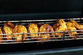 Saftige gegrillte Hähnchen, die auf einem Metallgestell garen, unterstreichen die lebhafte Street-Food-Szene auf einem Markt im Freien.