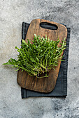A bunch of fresh rocket on a rustic wooden board with a dark cloth against a textured stone background. Perfect for natural and healthy food concepts.
