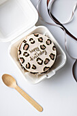 Top view of a South Korean bento cake with happy birthday icing in a white box to take away, complemented by a wooden spoon and a satin ribbon.
