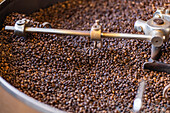 Close-up of freshly roasted coffee beans in an industrial roasting machine, capturing their rich colour and texture The machine processes large quantities smoothly