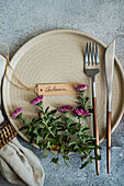 Elegantly laid table with a beige plate with a floral arrangement, a rustic nameplate labelled 'Autumn' and simple cutlery that reflects the charm of the season