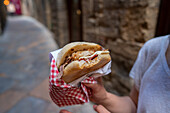 Close-up of a tasty panini in the charming streets of Volterra, Tuscany The delightful presentation includes a chequered paper wrapper that emphasises traditional Italian street food culture