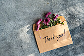 A brown envelope with bright pink flowers rests on a grey concrete surface The envelope contains a handwritten 'thank you' message expressing gratitude and appreciation
