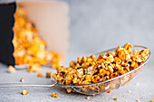 Sweet gourmet caramel popcorn in a shiny wire basket. The sugary, golden pieces dipped in caramel sit enticingly against a neutral grey background.