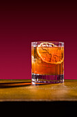 A classic old-fashioned whiskey cocktail served in a glass with an orange garnish The bright red background emphasises the strong amber tones of the drink, which is perfect for a variety of cocktail themes